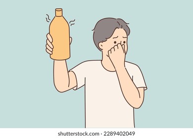 Man covers nose holding in hand bottle of drink or milk that has expired and begun to ferment. Young guy smells stench coming from bottle of gel with unpleasant flavor or toxic aroma