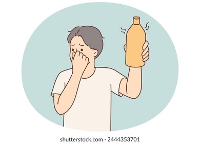 Man covers nose holding in hand bottle of drink or milk that has expired and begun to ferment. Young guy smells stench coming from bottle of gel with unpleasant flavor or toxic aroma