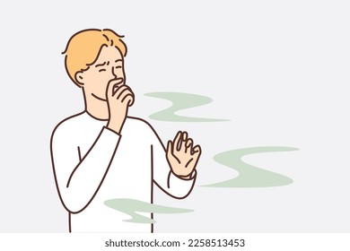 Man covers nose so as not to smell unpleasant smell from harmful production that pollutes environment. Guy grimaces and closes eyes, feels vile stench coming from missing products or garbage dump