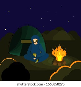 Man with dark beard in blue sport suit  with hood and yellow cup of tea on the camping at night. Bright character traveler on glade in forest  near beige tent and bonfire