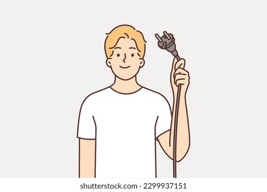 Man demonstrates wire with plug from electrical equipment, offering to turn off appliances for save energy. Young guy with smile offers to abandon use of electrical devices and take care of nature