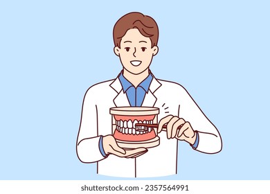 Man dentist explaining rules of brushing teeth, holding toothbrush and giant jaw in hands. Guy dentist recommends observing hygiene requirements to avoid appearance of caries in mouth