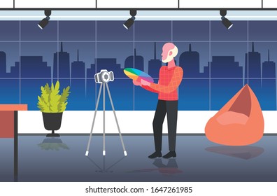man designer holding colored palette samples blogger recording online video with digital camera on tripod social network blogging concept modern design studio interior full length horizontal vector