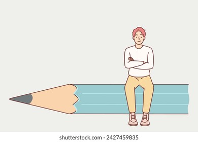 Man designer sits on giant pencil and crosses arms in front of chest, demonstrating confidence in own abilities. Successful guy designer in casual clothes smiles and looks at screen