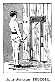 A man is doing chest exercise while pulling weights which are tied on machine with his arms. In this picture, he has pulled left string downwards while relaxing his right arm straight, vintage