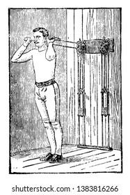 A man is doing exercise for chest expansion on machine by pulling weights using both of his arms straight. In this picture, he is not facing machine and repeating his left and right together, vintage