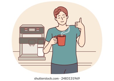 Hombre bebe café de la taza de pie cerca de la máquina para hacer delicioso espresso y muestra pulgares para arriba. Joven toma un descanso para tomar café para animarse y aumentar la productividad o mantenerse despierto haciendo un trabajo tedioso