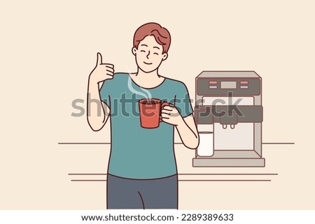 Man drinks coffee from mug standing near machine for making delicious espresso and shows thumbs up. Young guy takes coffee break to cheer up and increase productivity or stay awake doing tedious work 
