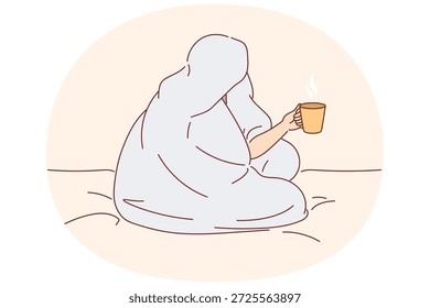 Man drinks coffee sitting on bed and wrapped in blanket to warm up after walk along winter street. Cup of hot coffee in hands of human enjoying comfort and energizing thanks to drink.