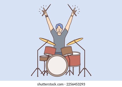 Man drummer member of youth rock band raise hands up starting performance in front of audience. Guy musician drummer sits among trommels getting ready for start of concert