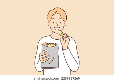 Man eats potato chips enjoying crispy high-calorie snack that quickly satisfies hunger. Smiling guy with potato chips is having lunch with harmful but tasty food containing cholesterol