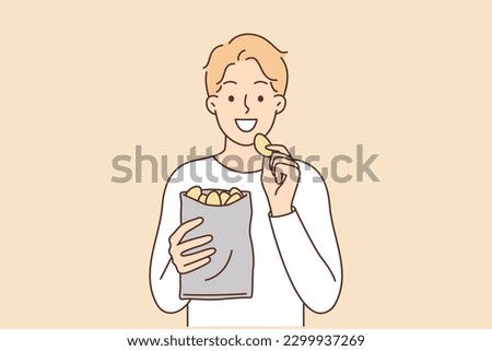 Man eats potato chips enjoying crispy high-calorie snack that quickly satisfies hunger. Smiling guy with potato chips is having lunch with harmful but tasty food containing cholesterol