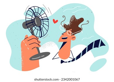 Man with electric fan in hand is trying to freshen up after returning from street in hot summer weather. Guy in business clothes uses fan due to lack of air conditioning in office.