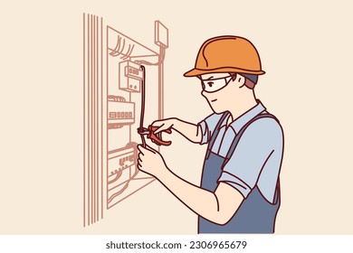 Man electrician repairs power shield and connects residential building or factory to electricity. Guy in electrician uniform repairs wiring standing near cabinet with power machines and wires