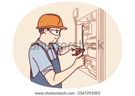 Man electrician repairs power shield and connects residential building or factory to electricity. Guy in electrician uniform repairs wiring standing near cabinet with power machines and wires