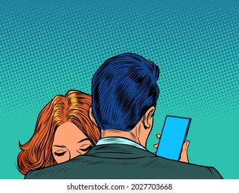 A man embraces a woman and looks at his smartphone