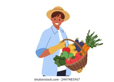 Man farmer holds basket of fresh vegetables in hands, rejoicing at excellent harvest, and smilingly looks at screen. Farmer guy in hat and gloves sells organic products filled with vitamins at fair