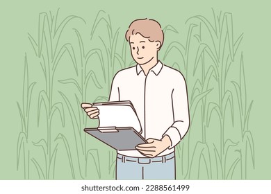 Man farmer inspecting corncobs standing in field with clipboard and working in agribusiness. Farmer in corn field controlling process of cultivating cereal plants to create organic products 
