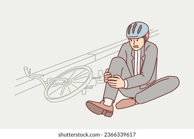 Man fell from bicycle and broke leg while commuting, and is sitting on ground waiting for doctor. Guy office worker got into accident on bicycle due to non-compliance with safety regulations