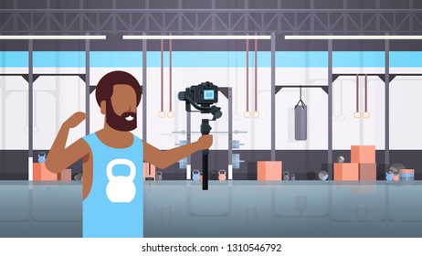 man fitness blogger shooting selfie video african american guy in front of camera recording himself using gimbal stabilizer blogging concept modern gym interior horizontal