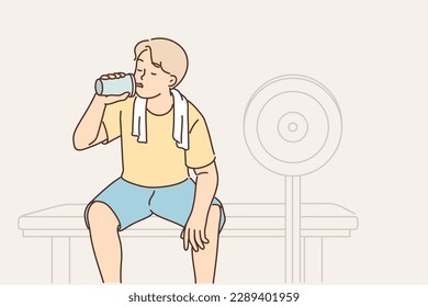 Man in fitness club and drinks protein shake from shaker to restore carbohydrate balance after grueling muscle-building workout. Guy training in gym sits on bench with barbell for fitness exercises 