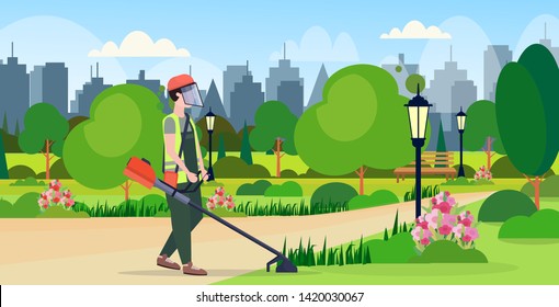 man gardener in uniform cutting grass with brush cutter gardening concept urban city park cityscape background flat full length horizontal