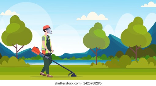 man gardener in uniform cutting grass with brush cutter gardening concept beautiful nature landscape background full length flat horizontal