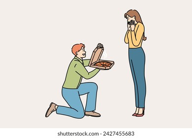 Man gives pizza to beloved, standing on knee and delighting girlfriend with fresh food from italian restaurant. Cheerful boyfriend proposes marriage to girl, with pizza instead of wedding ring