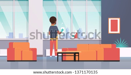 man in gloves and apron cleaning windows with rag cleaner spray rear view african american guy doing housework concept modern apartment living room interior flat full length horizontal