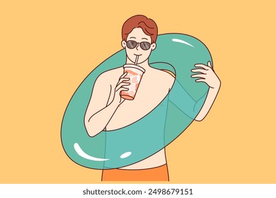 Man goes to beach and drinks cold cocktail, holding inflatable swimming ring in hand. Tourist guy enjoys relaxing near sunny pool at hotel and opportunity to sunbathe or swimming in warm sea