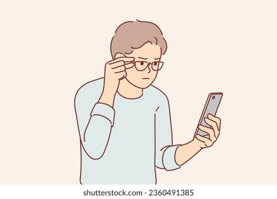 Man has vision problems and reads SMS message in small print on phone, adjusting glasses on eyes. Guy needs help of ophthalmologist to improve vision or replace eyeglasses to relieve myopia