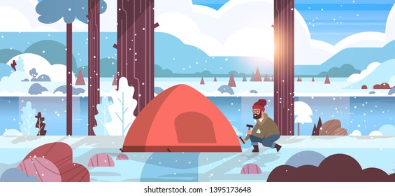 man hiker camper installing tent preparing for camping hiking concept sunrise winter snowfall landscape nature river mountains background flat horizontal full length