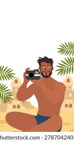man holding photo camera sitting beside sand castle beach
