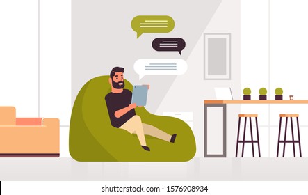man holding tablet chatting messaging guy sitting at bean bag using mobile app social network chat bubble communication concept modern living room interior full length horizontal vector illustration