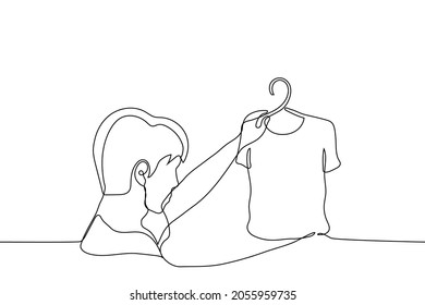 hombre con una camiseta delante de él en un perchero - un dibujo de una línea. nove man elige una camiseta para comprar 