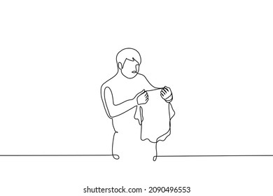 man holds and examines t-shirt one line drawing vector. concept of size clothes, stubborn stain on clothes 