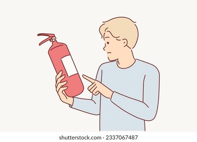 Man holds fire extinguisher checking expiration date of equipment for extinguishing flame in emergency. Guy controls quality of fire extinguisher, for concept of preventive measures to combat burning