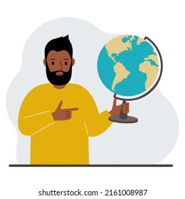 A man holds a globe in his hand and points his finger at it. The concept of education, teacher, world conquest, ecology.