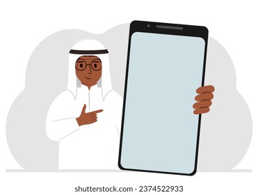 A man holds a mock-up of a large smartphone with a blank screen and with his second hand points to the screen of the phone.