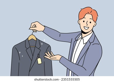 Man holds new jacket with tag offering to buy business clothes for managers or clerks. Guy works as salesman or dry cleaning employee and looks at screen with smile, giving client jacket on hanger