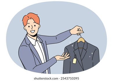 Hombre sostiene nueva chaqueta con etiqueta que ofrece comprar ropa de negocios para gerentes o empleados. El tipo trabaja como vendedor o empleado de limpieza en seco y mira la pantalla con sonrisa, dando chaqueta del cliente en la percha