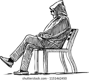 A man in a hood sits on a park bench