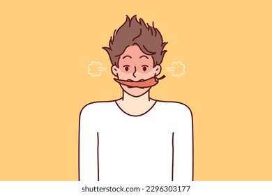 Man with hot chili or in teeth blushes and blows smoke from ears for metaphor of anger and negative emotions. Young guy with shaggy hair with hot chili pepper in mouth looks at screen