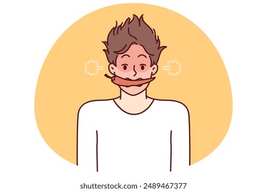 Man with hot chili or in teeth blushes and blows smoke from ears for metaphor of anger and negative emotions. Young guy with shaggy hair with hot chili pepper in mouth looks at screen