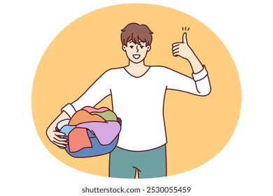 Man householder with laundry in basin shows thumbs up recommending quality laundry detergent. Guy getting ready to load textiles into washing machine setting positive example for peers