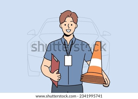 Man instructor from driving school smiles and holds traffic cones inviting to take exam for driver license. Guy employee of car school advertises services company teaching driving.