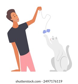 A man kneels and plays with a white cat using a string toy with a blue bow, both enjoying the moment.