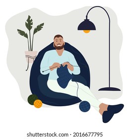 Man knits at cozy home sitting in bean lazy bag. Person create wool clothes. Hobby time, crocheting. Cozy living room or apartment with beanbag chair, plant, lamp