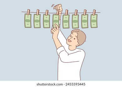 Man laundering money received from illegal business hangs banknotes on rope and rejoices at enrichment. Guy is involved in money laundering from criminal activities, or counterfeiting cash.