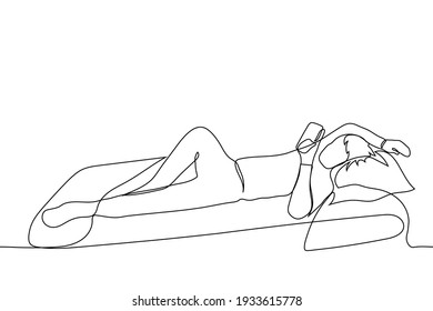 man lies holding a phone in his hands, his other hand is resting on the pillow, his leg is bent at the knee - one line drawing. the concept of mobile online surfing lying in bed before going to bed